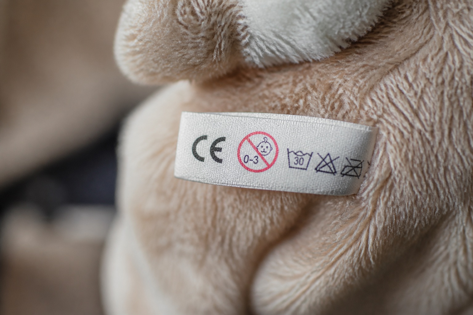 Nahaufnahme eines Anhängers an einem Kuscheltier mit CE-Zeichen, Altersangabe und Pflegesymbolen